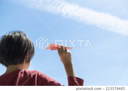 A child holding a paper airplane with a contrail and blue sky 123578485