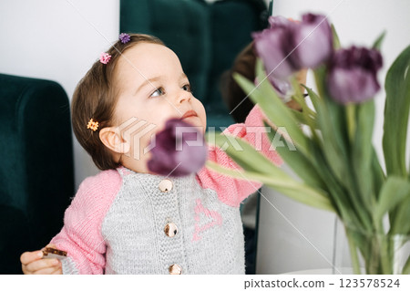 Toddler girl reaching for purple tulips with curiosity. Early childhood exploration, sensory play, nature interaction, indoor playtime, child development Toddler girl reaching for purple tulips with curiosity. Early childhood exploration, sensory play, nature interaction, indoor playtime, child development 123578524