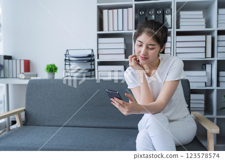 Woman is sitting on a couch using a smartphone and engaging in social media while enjoying a relaxing moment at home 123578574