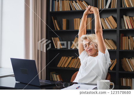 Middle aged senior woman relaxing stretching arms and body taking break from work on laptop at home. Older mature woman happy after work done satisfied by good result. Fatigue from long laptop usage 123578680