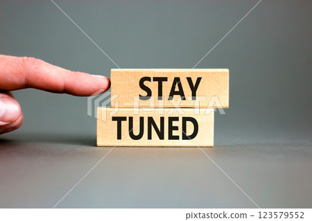 Stay tuned symbol. Concept words Stay tuned on wooden blocks on a beautiful grey table grey background. Businessman hand. Business, support, motivation, psychological stay tuned concept. Copy space. Stay tuned symbol. Concept words Stay tuned on wooden blocks on a beautiful grey table grey background. Businessman hand. Business, support, motivation, psychological stay tuned concept. Copy space. 123579552