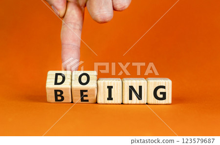 Doing or being symbol. Concept word Doing and Being on wooden cubes. Businessman hand. Beautiful orange table orange background. Business doing or being concept. Copy space. 123579687