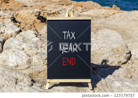 Tax year end symbol. Concept words Tax year end on beautiful black yellow blackboard. Beautiful stone and blue sea sky background. Business tax year end concept. Copy space. Tax year end symbol. Concept words Tax year end on beautiful black yellow blackboard. Beautiful stone and blue sea sky background. Business tax year end concept. Copy space. 123579787