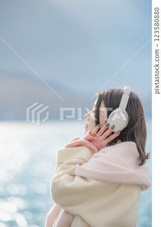 Young woman listening to music on headphones by the lake 123580880