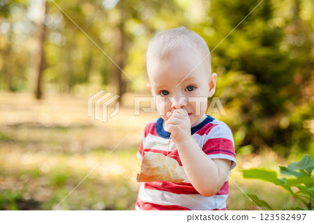 Portrait of a one-year-old boy in a red and white striped shirt against a sunny park background 123582497