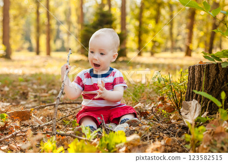 Little boy under one year old sitting on a tree stump in the park playing with a dry twig 123582515