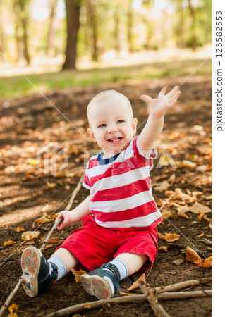 One-year-old baby playing with natural materials leaves and twigs in a warm autumn forest 123582553
