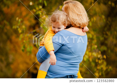 Loving mother holding toddler girl with curly hair in yellow shirt in autumn park Loving mother holding toddler girl with curly hair in yellow shirt in autumn park 123582860