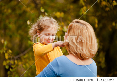 Loving mother holding toddler girl with curly hair in yellow shirt in autumn park Loving mother holding toddler girl with curly hair in yellow shirt in autumn park 123582862