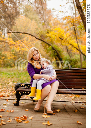 Plus-size woman in purple dress gently hugging her crying 3-year-old daughter on a bench in an autumn park 123582878
