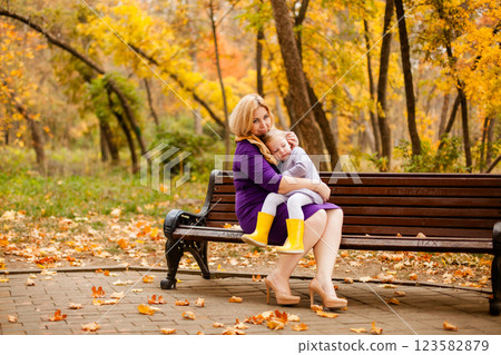 Loving mother in purple dress hugging her sad daughter on park bench Loving mother in purple dress hugging her sad daughter on park bench 123582879