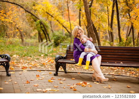 Loving mother in purple dress hugging her sad daughter on park bench 123582880