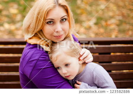 Loving mother in purple dress hugging her sad daughter on park bench 123582886