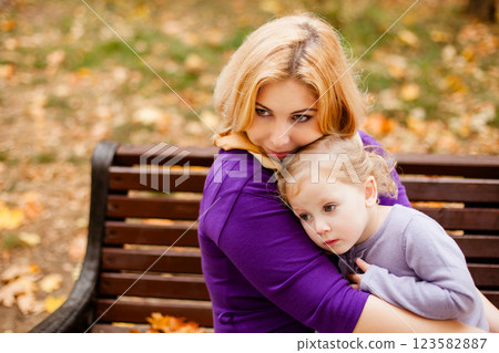 Loving mother in purple dress hugging her sad daughter on park bench Loving mother in purple dress hugging her sad daughter on park bench 123582887