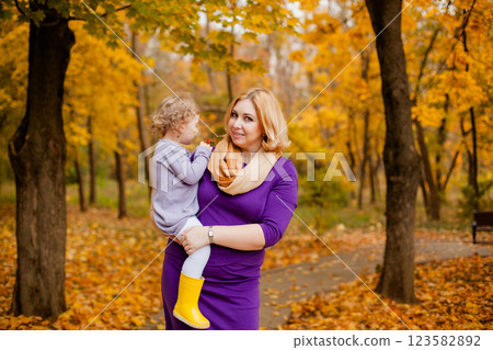 Plus-size woman in purple dress holding and playing with her 3-year-old daughter in autumn park Plus-size woman in purple dress holding and playing with her 3-year-old daughter in autumn park 123582892