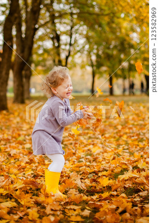 Toddler girl in purple dress, white tights, and yellow rubber boots playing happily with leaves in autumn park Toddler girl in purple dress, white tights, and yellow rubber boots playing happily with leaves in autumn park 123582969