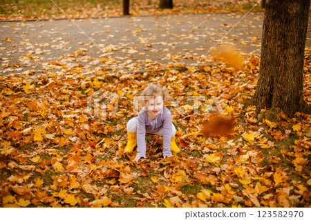 Toddler girl in purple dress, white tights, and yellow rubber boots playing happily with leaves in autumn park Toddler girl in purple dress, white tights, and yellow rubber boots playing happily with leaves in autumn park 123582970