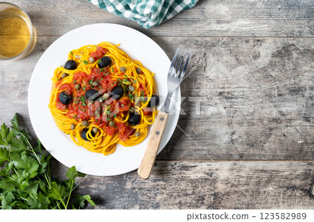 Italian Pasta puttanesca with tomato sauce, capers, and black olives on wooden table. Top view. Copy space 123582989