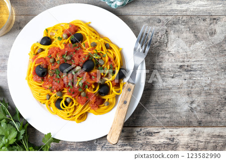 Italian Pasta puttanesca with tomato sauce, capers, and black olives on wooden table. Top view. Copy space Italian Pasta puttanesca with tomato sauce, capers, and black olives on wooden table. Top view. Copy space 123582990