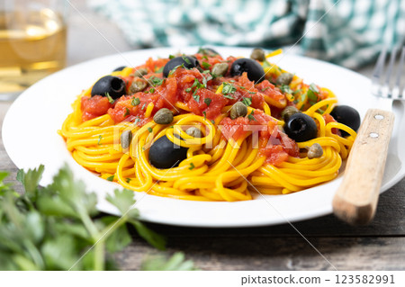 Italian Pasta puttanesca with tomato sauce, capers, and black olives on wooden table 123582991