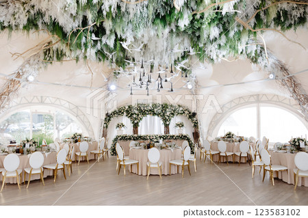 Elegant wedding reception hall featuring round tables, white and gold chairs, and floral arrangements 123583102