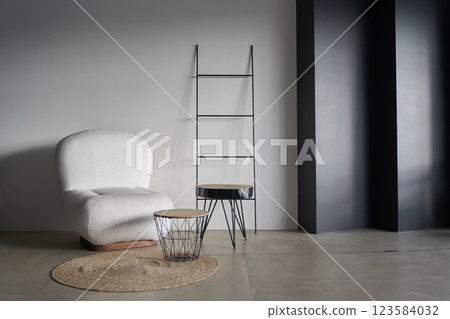 Modern design of the living room with a white armchair on the background of a black uneven wall in the form of steps. A metal ladder completes the design. With space to copy. High quality photo 123584032
