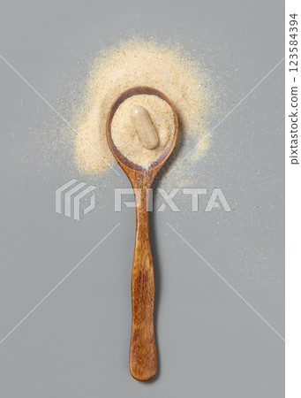 Wooden spoon full of beige powder and capsule on grey top view. Dietary supplement or kitchen spice 123584394