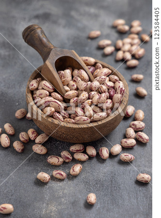 Wooden bowl full of dried pinto beans with scoop on gray closeup. Traditional Latin American legumes 123584405