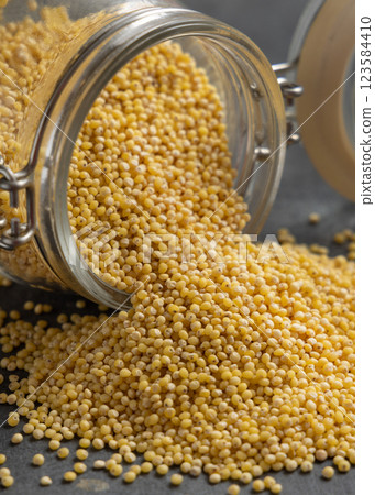 Glass jar of raw yellow pearl hulled millet grain on grey table closeup. Ancient food Glass jar of raw yellow pearl hulled millet grain on grey table closeup. Ancient food 123584410