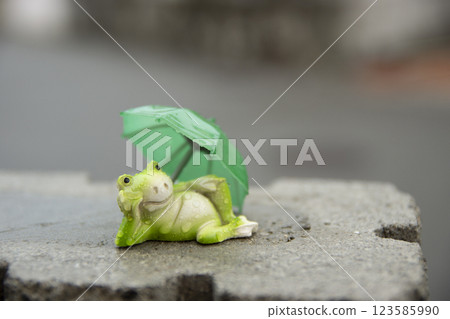 A rain-soaked frog and an umbrella relaxing on a wall 123585990