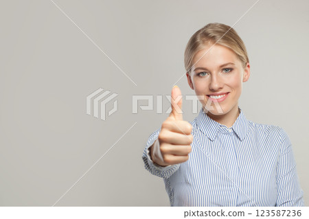 Successful business woman looking at camera, smiling and holding thumb up on grey background 123587236