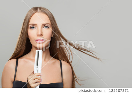 Indoor portrait of brunette woman holding straight hair iron Indoor portrait of brunette woman holding straight hair iron 123587271
