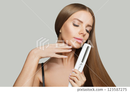 Glorious smiling woman with long straight healthy hairstyle using straightening iron  123587275