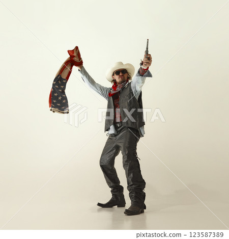 Fearless man, cowboy in white hat, gripping revolver in one hand and waving American flag, standing proud with determined stance. Fearless man, cowboy in white hat, gripping revolver in one hand and waving American flag, standing proud with determined stance. 123587389