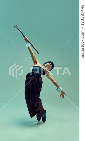 Sophisticated presence captured mid-motion, man freezes in theatrical jump with impeccable form, bow tie and vintage styling against green background. 123587448