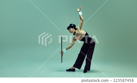 Graceful man bending dramatically while extending cane, embodying old-world charm in pinstriped trousers and corset against muted green backdro 123587458