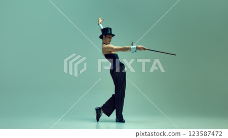 Stylish dancer in high-waisted corset and classic top hat extending cane with theatrical presence against muted green studio background. Concept of retro glamour Stylish dancer in high-waisted corset and classic top hat extending cane with theatrical presence against muted green studio background. Concept of retro glamour 123587472