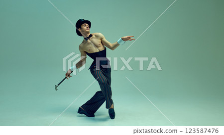 Graceful male dancer in vintage-inspired corset suit dynamically stepping with cane against muted green studio background. Concept of classic fashion Graceful male dancer in vintage-inspired corset suit dynamically stepping with cane against muted green studio background. Concept of classic fashion 123587476