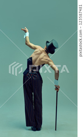 Rear view of elegant male performer in fitted corset and top hat arching back with graceful movement against muted green studio background. Rear view of elegant male performer in fitted corset and top hat arching back with graceful movement against muted green studio background. 123587481