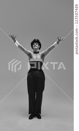 Refined performer in corset and classic top hat gesturing gracefully with theatrical presence against muted green studio background. Refined performer in corset and classic top hat gesturing gracefully with theatrical presence against muted green studio background. 123587489