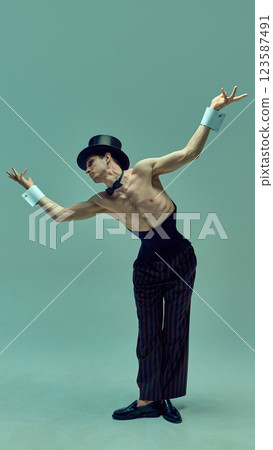 Charismatic figure in pinstriped corset suit and dramatic hat spreading arms in celebratory stance against green background. Charismatic figure in pinstriped corset suit and dramatic hat spreading arms in celebratory stance against green background. 123587491