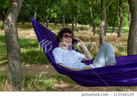 A young guy with curly hair is relaxing on a hammock on a hot summer day. A young guy with curly hair is relaxing on a hammock on a hot summer day. 123588129