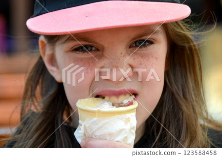 Close up image of girl hand holding fresh waffle cone with vanilla and raspberry ice cream on the wooden background. Walking. Outdoors. High quality photo. High quality photo 123588458