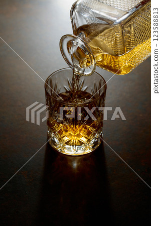 Whiskey pour from a decanter into a cut glass tumbler. Whiskey pour from a decanter into a cut glass tumbler. 123588813