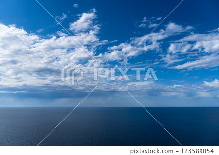 A tranquil blue ocean meets a serene sky adorned with soft, fluffy clouds on a sunny day. 123589054