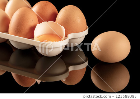 Reflective black surface with brown chicken eggs in the background 123589383