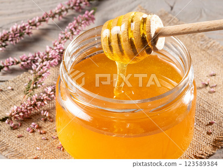 Jar of heather honey and honey dipper on rustic tabletop - natural sweetener concept 123589384