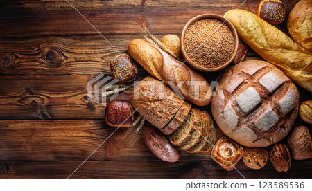 Bread and rolls background with different bakery food on old wooden table with copy space for advertising. Group of home cooking made of whole wheat and grain. Baked goods texture 123589536