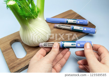 Hands holding Insulin injection pen and fennel vegetable root for diabetics and weight loss. 123589585