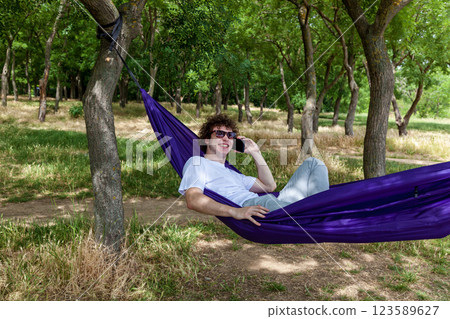 A young guy with curly hair is relaxing on a hammock on a hot summer day. 123589627